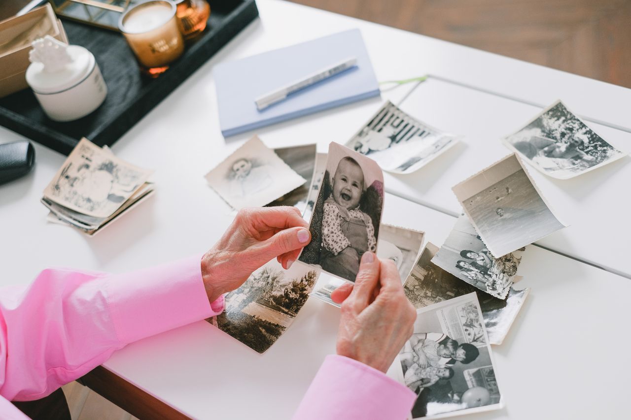 A person in a pink shirt organizing old black and white family photos on a table.